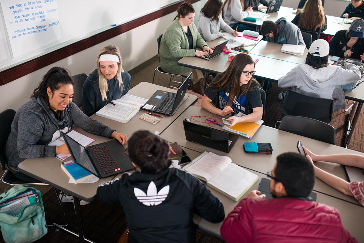 一群学生面对面坐在教室里，用电脑聊天.